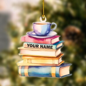May include: A stack of colorful books with a blue teacup and saucer on top. The books have a watercolor effect and the top book has the text "YOUR NAME" printed on it. This is a personalized ornament.
