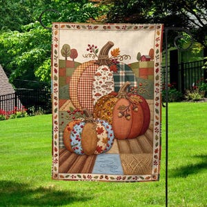 May include: A rectangular garden flag featuring a patchwork-style illustration of three pumpkins with varied patterns including gingham, mushrooms, and leaves. The design includes red berries and acorns, set against a landscape with a small red barn.