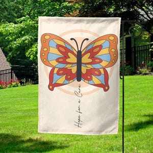 Puede incluir: Una bandera de jardín con un diseño de mariposa colorido y el texto "Hope for a Cure".