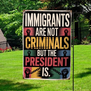 May include: A rectangular garden flag with the text "IMMIGRANTS ARE NOT CRIMINALS BUT THE PRESIDENT IS." The flag has a distressed look with a black background and colorful stripes. The flag is hanging on a black metal stand in a grassy yard.