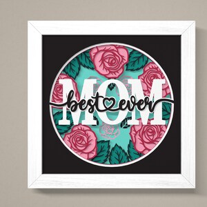 May include: White framed art print with a black background and a circle in the centre. The circle has a turquoise background with pink roses and green leaves. The text "MOM best ever" is in white with a pink heart in the middle of the word "best".