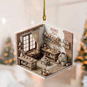 May include: A clear, square ornament depicting a pottery studio with wooden tables, shelves, and a window. The scene includes various pottery pieces, tools, and the text "NAME 2025". The ornament is suspended by a gold cord.