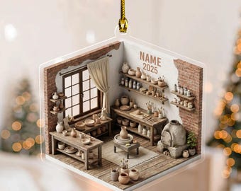 May include: A clear, square ornament depicting a pottery studio with wooden tables, shelves, and a window. The scene includes various pottery pieces, tools, and the text "NAME 2025". The ornament is suspended by a gold cord.