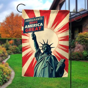 May include: A garden flag featuring a vintage-style illustration of the Statue of Liberty holding a sign that reads "IMMIGRANTS MAKE AMERICA GREAT." The background has a red and cream sunburst design.