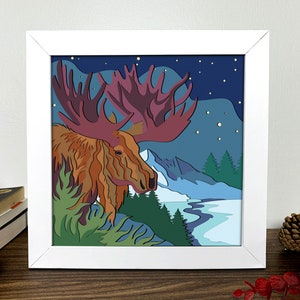 May include: A framed illustration of a moose with large antlers standing in a snowy forest landscape under a starry night sky.