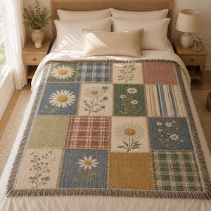 May include: A woven throw blanket featuring a patchwork design of various squares. The pattern includes floral motifs with white daisies, blue and green plaid squares, striped sections, and solid blocks in muted tones of green, blue, and gold.