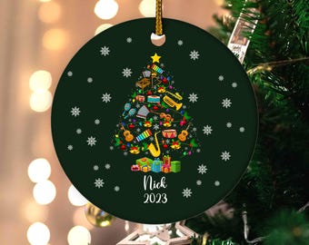 May include: A dark green Christmas ornament with a musical instrument-themed tree design. The tree is decorated with various instruments, lights, and a star. The name "Nick" and the year "2023" are printed on the ornament.