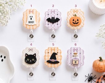 May include: Six badge reels with scalloped edges and small bows, featuring Halloween icons: a white ghost with the text BOO!, a black bat, an orange jack-o'-lantern, a black cat face, a black witch hat, and a purple potion bottle labeled POISON.