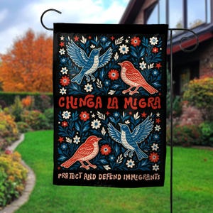 May include: Black garden flag with a design featuring four birds in blue and red, surrounded by flowers and foliage. The flag has the text "CHINGA LA MIGRA" and "PROTECT AND DEFEND IMMIGRANTS" in white.
