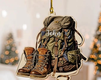 May include: Wooden ornament featuring a backpack and hiking boots. The backpack is brown and green with the name "John" on it. The boots are brown with laces. A gold string is attached for hanging.