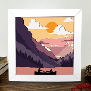May include: A framed illustration of a couple in a boat on a lake surrounded by mountains. The sky is a gradient of orange, pink, and purple with white clouds and a bright orange sun.