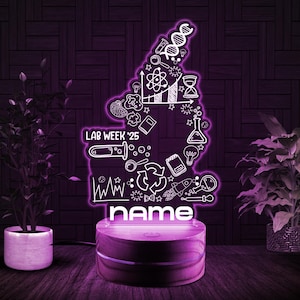May include: A white neon sign with a science theme, including a DNA strand, a beaker, a lightbulb, and the text "LAB WEEK '25". The sign is on a wooden base with the word "name" below it.