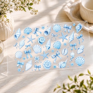 May include: A clear sticker sheet featuring a collection of light blue illustrations of various seashells, starfish, small flowers, and decorative ribbons arranged across the surface in a repeating pattern with a soft, watercolor-like aesthetic.