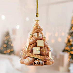 May include: A clear acrylic Christmas tree ornament shaped like a tree made of various types of bread. The ornament is decorated with string lights and a gold star. The word "NAME" is printed on the bottom bread.