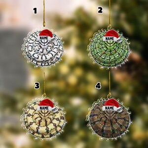 May include: Four Christmas ornaments featuring snake designs. Each ornament has a different snake pattern and is wearing a Santa hat with the text "NAME" and "2025". The ornaments are hanging from gold strings.