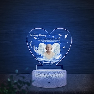 May include: A heart-shaped memorial night light with a photo of a woman with angel wings, the text "In Loving Memory," and the name "Grandma Gwen" with the years 1960-2024. The light has a blue base and a clear acrylic heart.