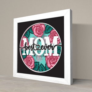 May include: White framed wall art with a black background and a circle featuring a floral design with pink roses and green leaves. The text "best mom ever" is written in black cursive with a heart symbol.