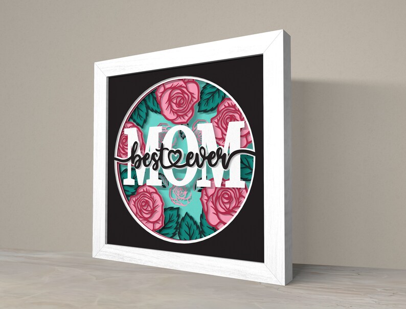May include: White framed wall art with a black background and a circle featuring a floral design with pink roses and green leaves. The text "best mom ever" is written in black cursive with a heart symbol.