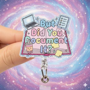 May include: A glittery badge reel with the text "But Did You Document It?" features a laptop, tablet, and a bubble tea cup illustration. The design is set against a pink book, with stars and sparkles. The reel has a silver clip and a clear plastic base.