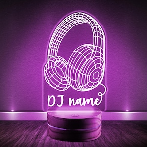 May include: A white LED night light shaped like headphones with the text "DJ name" below. The light is on a wooden base.