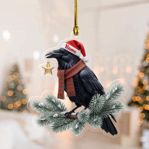 May include: A Christmas ornament featuring a black crow wearing a Santa hat and a red and green plaid scarf. The crow is perched on a snowy pine branch and holding a gold star. The word "Name" is printed on the hat.