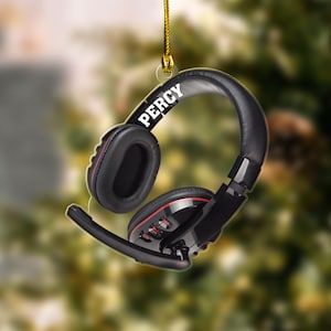 May include: A black and red headset ornament with the name "PERCY" in white lettering. The headset has a microphone and is suspended by a gold string, suggesting a holiday decoration.