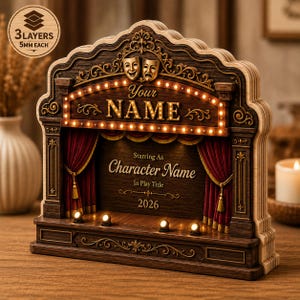 May include: A layered wooden theater display featuring a marquee with the text Your NAME, comedy and tragedy masks, and red curtains. The stage includes the text Starring As Character Name, In Play Title, and 2026. A circular badge notes 3 LAYERS 5MM EACH.