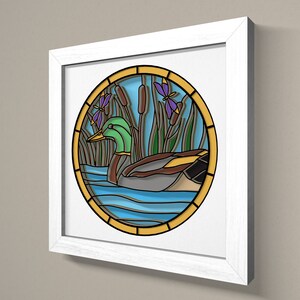 May include: A framed stained glass artwork depicting a green duck swimming in a blue pond with green reeds and purple dragonflies. The artwork is surrounded by a yellow border.