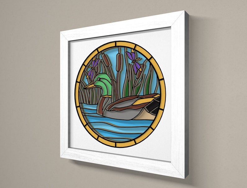 May include: A framed stained glass artwork depicting a green duck swimming in a blue pond with green reeds and purple dragonflies. The artwork is surrounded by a yellow border.