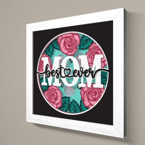May include: White framed wall art with a black background and a circle in the centre. The circle has a turquoise background with pink roses and green leaves. The text "MOM best &hearts; ever" is in black lettering.