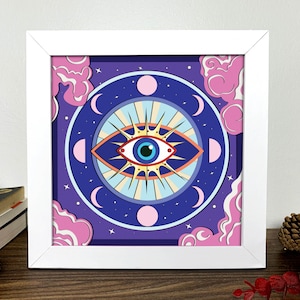 Pode incluir: Uma impressão emoldurada com uma ilustração colorida de um olho grande com uma íris azul e uma pupila amarela. O olho é cercado por um círculo de luas crescentes rosa e azuis e estrelas em um fundo roxo.