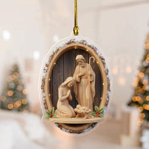 May include: A Christmas ornament featuring a Nativity scene. The ornament has a wooden frame with a snowy edge. Inside, carved figures of Mary, Joseph, and baby Jesus are depicted. The ornament is suspended by a gold cord.
