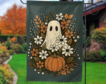 May include: A dark teal garden flag featuring a friendly ghost surrounded by flowers and a pumpkin. The ghost is white with black eyes and a mouth. The flowers are white and orange, and the pumpkin is orange. The flag is hanging on a black metal stand.