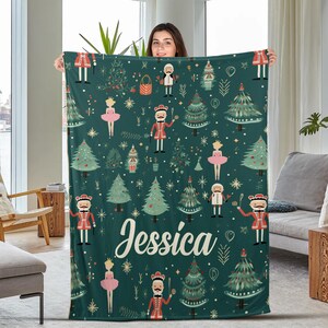 May include: A green fleece blanket with a festive Nutcracker theme. The blanket features a repeating pattern of Nutcracker characters, Christmas trees, and stars. The name "Jessica" is printed in a white cursive font on the blanket.