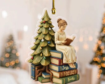 May include: A Christmas tree ornament featuring a woman reading a book while seated on a stack of books. The ornament has a Christmas tree on the left side. The text on the books reads "Jess", "Just a girl who loves", and "Books".