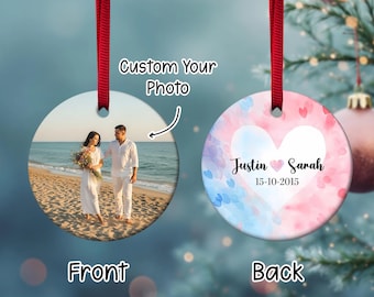 May include: A round, white Christmas ornament with a red ribbon. One side features a couple on a beach, the other side has a heart design with names and a date. Text reads "Custom Your Photo", "Front", and "Back".