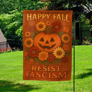 May include: A decorative garden flag with a fall theme. The flag features a smiling jack-o'-lantern surrounded by sunflowers and other fall flowers. The words "HAPPY FALL" and "RESIST FASCISM" are printed on the flag in orange lettering against a brown background.