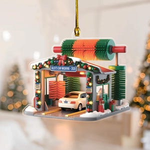 May include: A Christmas ornament depicting a car wash scene. The ornament features a white car inside the car wash, with red, green, and white detailing. The text "Alex's Car Washing - 202X" is visible on the sign.