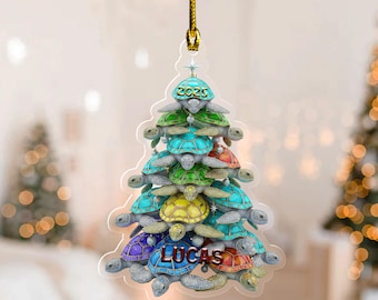May include: A Christmas tree ornament shaped like a tree, made of colorful sea turtles. The top turtle has the year 2025 on it, and the name "LUCAS" is at the bottom. The ornament hangs from a gold string.