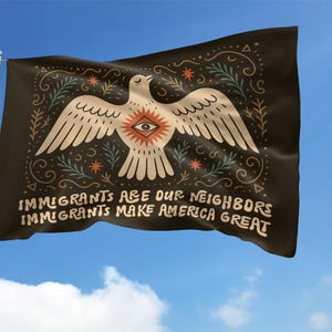 May include: A black flag waving in the wind against a blue sky. The flag features a white dove with an eye in the center, surrounded by decorative elements. Text on the flag reads, "IMMIGRANTS ARE OUR NEIGHBORS, IMMIGRANTS MAKE AMERICA GREAT."