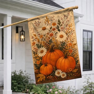 May include: A rectangular garden flag featuring a printed illustration of three orange pumpkins arranged on a wooden surface, surrounded by white daisies, orange wildflowers, and autumn foliage against a warm, textured beige background.