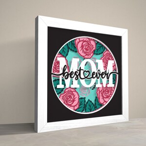May include: White framed picture with a black background and a circle in the centre. The circle has a turquoise background with pink roses and green leaves. The text "best ever" is written in black with a heart in the middle of the word "best". The word "MOM" is written in white letters around the circle.
