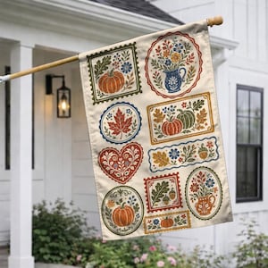 May include: A rectangular garden flag featuring a cream-colored background with various framed illustrations including orange pumpkins, red maple leaves, blue flowers, green oak leaves, and acorns arranged in circular, heart, and rectangular shapes.