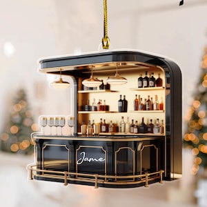 May include: A black and gold bar ornament with the name "Jame" in script. The ornament features a bar with shelves of liquor bottles, glasses, and hanging lights. A gold cord is attached for hanging.