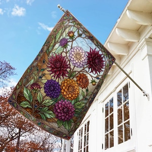 May include: A rectangular garden flag featuring a stained glass style illustration of vibrant dahlias in shades of deep red, purple, orange, and pale pink, surrounded by green leaves and intricate dark brown vine-like borders on a light background.