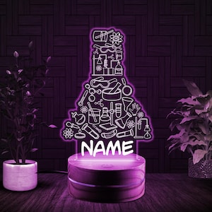 May include: A purple LED night light shaped like a science beaker, featuring white line art of lab equipment. The base is a wooden circle with the word "NAME" in white. The light is on a dark purple background.