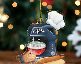 May include: A blue and white ornament featuring a stand mixer, chef's hat, rolling pin, and bowl of cream. The name "Alita" is written on the mixer. A gold string is attached for hanging. The ornament is designed for baking enthusiasts.