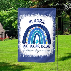 May include: A blue garden flag with a rainbow design and the text "In April We Wear Blue Autism Awareness".