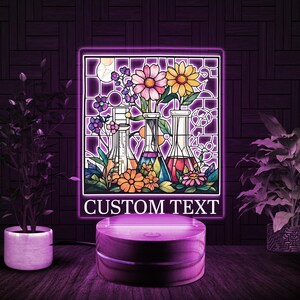 May include: A stained glass style night light with a floral design and four glass bottles. The night light has a wooden base and the text "CUSTOM TEXT" is displayed below the image.