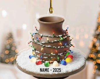 May include: A brown ceramic vase Christmas ornament, adorned with colorful string lights and faux snow. The ornament has a gold string for hanging and the text "NAME - 2025" at the bottom. Festive holiday decor.